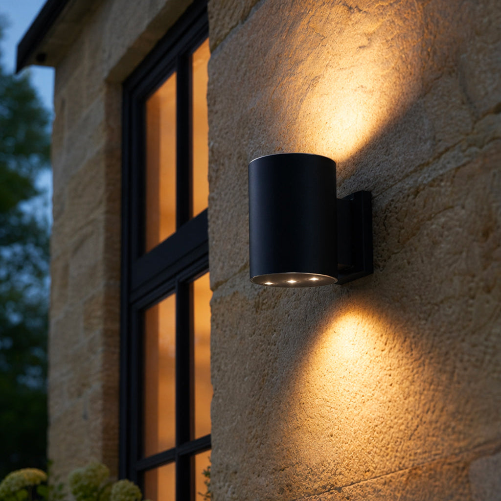 Black outdoor wall light fixture on a stone building exterior.